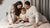 In the photo you can see the whole family – mom, dad, and a toddler – sitting on a bed, reading a book. They are all wearing natural color matching two-piece pajamas made from organic 100% Merino wool.