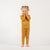 A young child with curly blonde pigtails, wearing a yellow long-sleeved top and matching pants, stands barefoot on a white background, looking directly at the camera with a gentle smile.