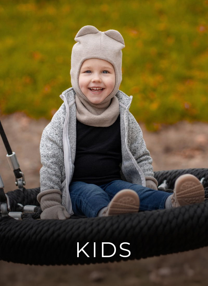 Child wearing a cozy outfit with a hood and scarf, sitting in a stroller outdoors.