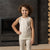 A young child with light curly hair in pigtails is sitting on a white surface against a plain white background. The child is wearing a menique sleeveless top and matching leggings. They are looking directly at the camera with a pouty expression, and their bare feet are visible.
